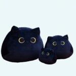 Three black plush cats of three different sizes. Placed on a wooden table.