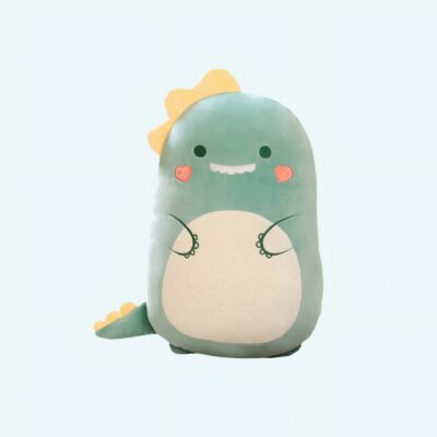 Soft Squishmallow plush shaped like a green dinosaur with a beige belly, pink cheeks, and a sweet smile. It features cute details like a yellow crest on its head and a yellow-spiked tail, making it extra cuddly and lovable.